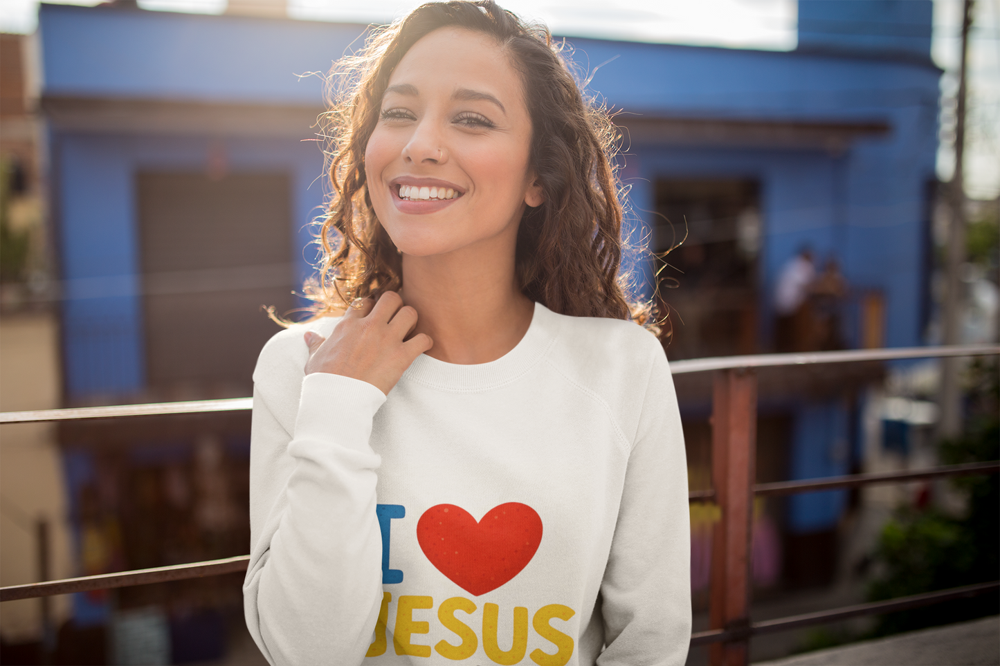 Woman wearing a white sweatshirt with 'I ❤️ JESUS' text, standing in front of a blue building.